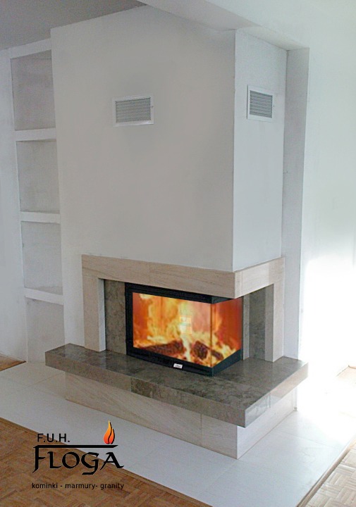 Nowoczesny kominek narożny z obudową z jasnego kamienia i płomieniami widocznymi przez szklaną szybę, z logo firmy Floga w dolnej części zdjęcia.