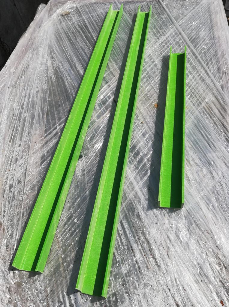 Trzy zielone, profilowane elementy stalowe ułożone na przezroczystej folii budowlanej.