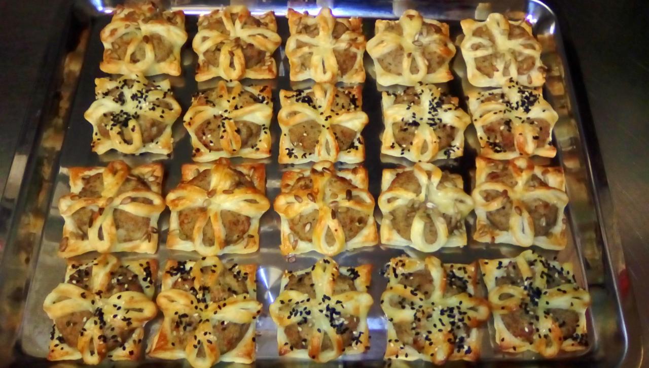 Blacha z kwadratowymi pasztecikami z mięsem, udekorowanymi ciastem francuskim i posypanymi sezamem.