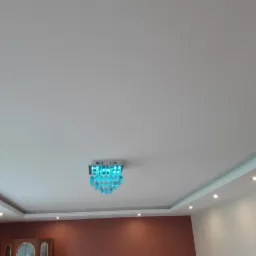 Biały sufit z dekoracyjnym oświetleniem LED w kolorze turkusowym i wpuszczanymi punktowymi lampami halogenowymi, widoczny fragment ściany pomalowanej na brązowo