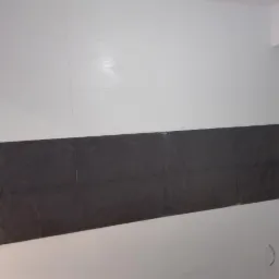 Ściana w łazience z białymi i czarnymi płytkami ułożonymi w pasy, widoczne niedociągnięcia przy oknie i wystające przewody.