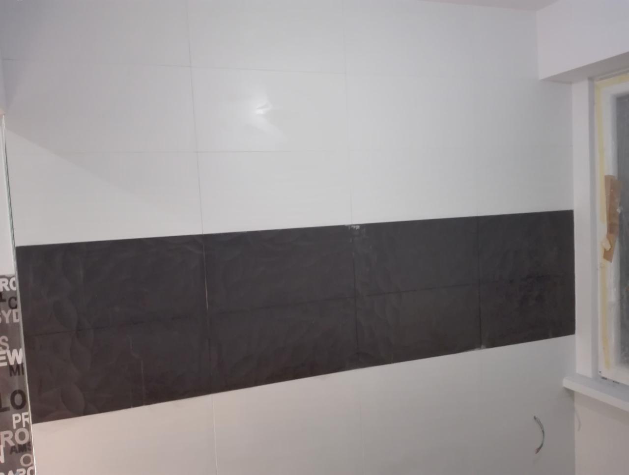 Ściana w łazience z białymi i czarnymi płytkami ułożonymi w pasy, widoczne niedociągnięcia przy oknie i wystające przewody.