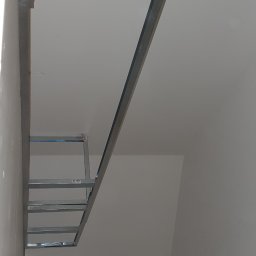 Uslugi bud - Metalowa konstrukcja sufitu podwieszanego w trakcie montażu, widoczna drabina malarska, surowy stan wykończenia.