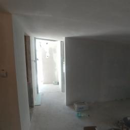 Uslugi bud - Surowe wnętrze mieszkania w trakcie prac wykończeniowych, widoczne ślady szpachlowania na ścianach i sufitach, przygotowane do dalszych etapów, z otwartym przejściem do kolejnego pomieszczenia