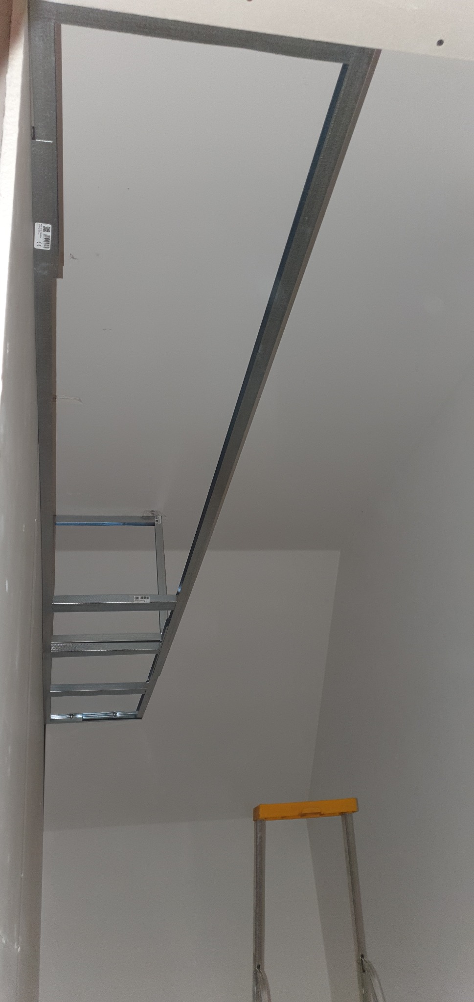 Metalowa konstrukcja sufitu podwieszanego w trakcie montażu, widoczna drabina malarska, surowy stan wykończenia.