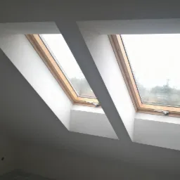 Dwa okna dachowe z drewnianymi ramami, w białej zabudowie z płyt karton gips, widok na zewnątrz w pochmurny dzień, wykończone gładzią i pomalowane na biało.