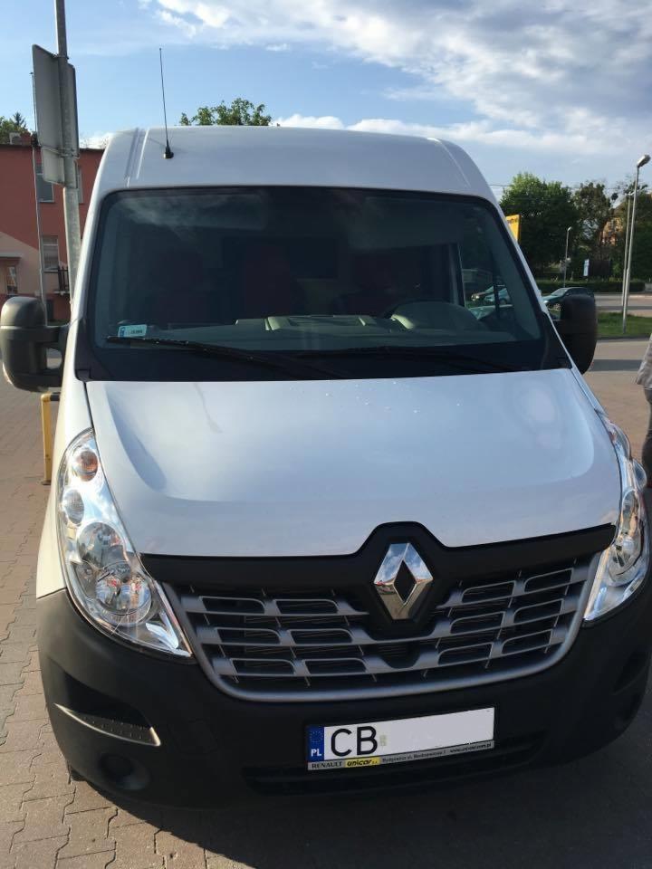 Biały samochód dostawczy Renault Master z polską tablicą rejestracyjną, zaparkowany na chodniku przed budynkiem w słoneczny dzień.