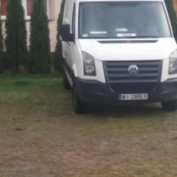 Biały van Volkswagen Crafter zaparkowany na trawniku przed domem z czerwoną dachówką, widok z przodu.