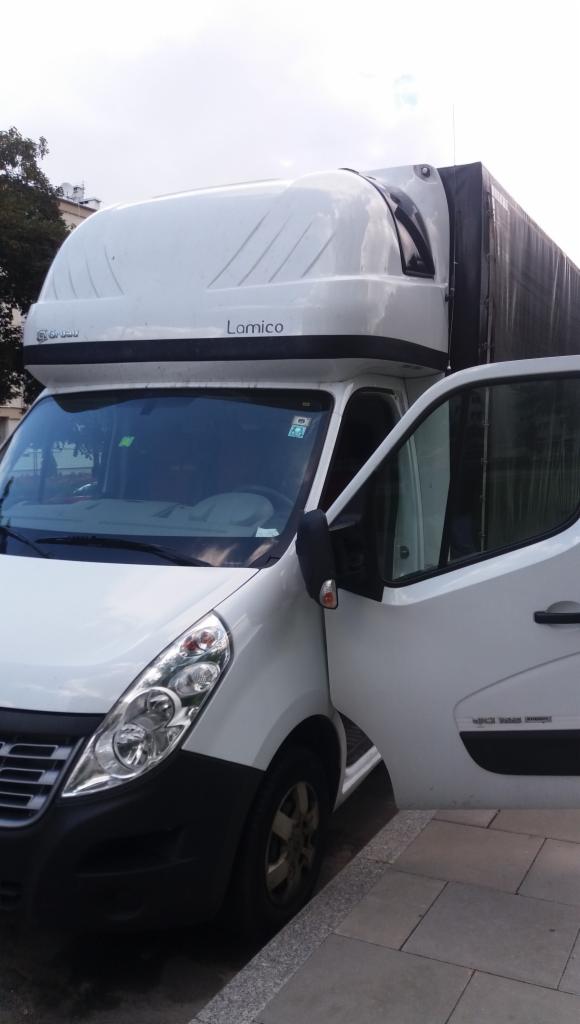 Biały samochód dostawczy marki Renault z otwartymi drzwiami kierowcy, widoczny napis 'Lomico' na nadbudówce, zaparkowany na chodniku.