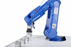 Niebieski robot przemysłowy Yaskawa precyzyjnie umieszcza białe, sześcienne elementy, każdy z wytłoczonym napisem VIPA, na białej powierzchni roboczej.