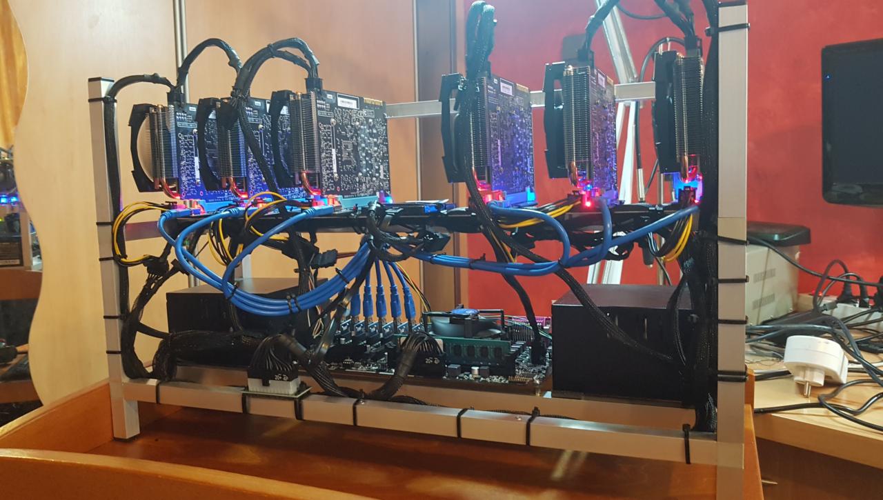 Rzędowy układ kart graficznych z chłodzeniem, zamontowanych na stelażu z aluminiowych profili, z widocznym okablowaniem i płytą główną w tle, na biurku w pomieszczeniu z czerwonymi ścianami.