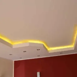 Sufit podwieszany z oświetleniem LED w ciepłym odcieniu, wkomponowany w nowoczesne wnętrze z fragmentem czerwonej ściany.