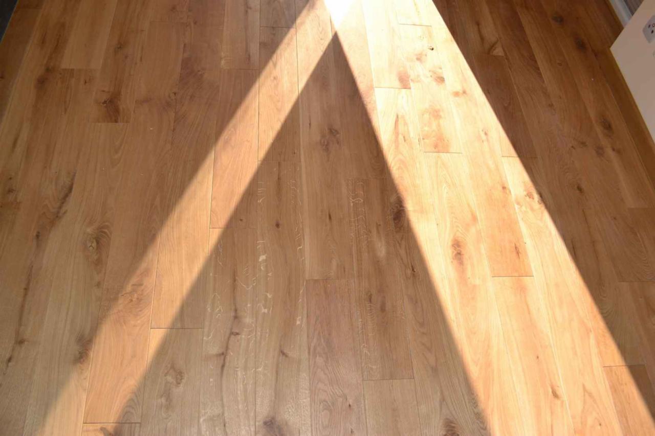 Jasna, dębowa podłoga parkietowa w świetle słonecznym, z widocznym wzorem słojów i delikatnymi refleksami światła.