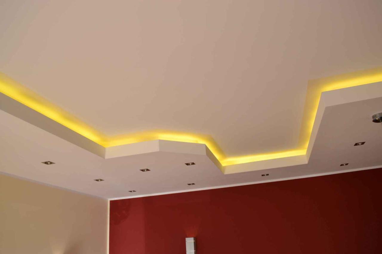 Sufit podwieszany z oświetleniem LED w ciepłym odcieniu, wkomponowany w nowoczesne wnętrze z fragmentem czerwonej ściany.