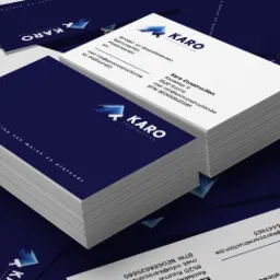 Stos wizytówek firmy budowlanej Karo Construction z ciemnoniebieskim tłem i białym tekstem, prezentujących logo i dane kontaktowe.