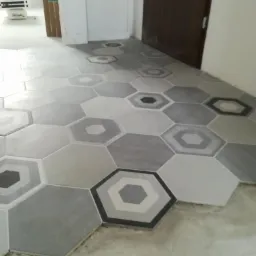 Układanie heksagonalnych płytek podłogowych w odcieniach szarości na surowym podłożu, widoczne niedociągnięcia fugowania.