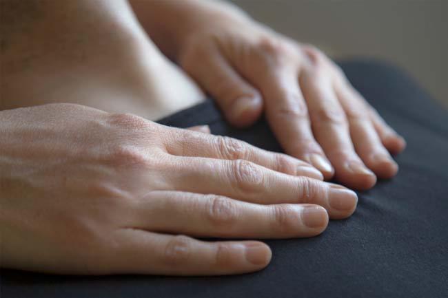 Dłonie spoczywają delikatnie na ciemnym materiale, sugerując sesję relaksacyjną lub energetyczną, z widocznymi subtelnymi detalami skóry dłoni.