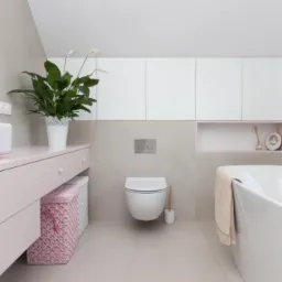 Jasna łazienka w stylu minimalistycznym z wiszącą toaletą, różową szafką z koszami z wikliny, białą wanną i szafkami pod sufitem.