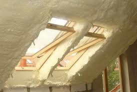 Poddasze z oknami dachowymi po izolacji natryskowej, widoczna struktura piany wypełniająca przestrzeń wokół ram okiennych.