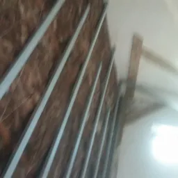 Ściana w trakcie ocieplania, widoczne metalowe profile pionowe i brązowa wełna mineralna, w tle fragment okna i konstrukcja dachu. Zdjęcie wykonane pod kątem, z bliska.