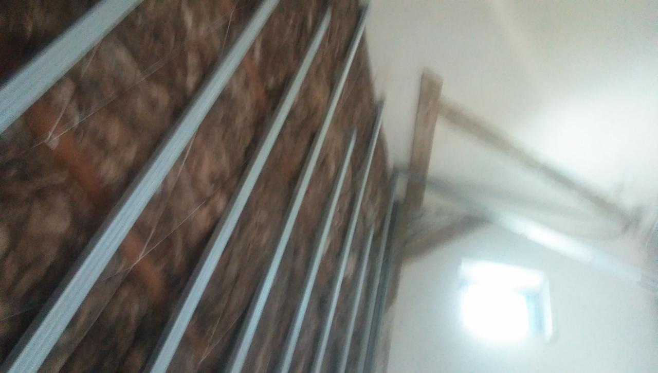 Ściana w trakcie ocieplania, widoczne metalowe profile pionowe i brązowa wełna mineralna, w tle fragment okna i konstrukcja dachu. Zdjęcie wykonane pod kątem, z bliska.