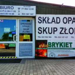 Fasada budynku firmy Ekologika s.c. oferującej sprzedaż opału, skup złomu oraz sprzedaż brykietu drzewnego EkoBrykiet, z widocznymi godzinami otwarcia i numerami telefonów.
