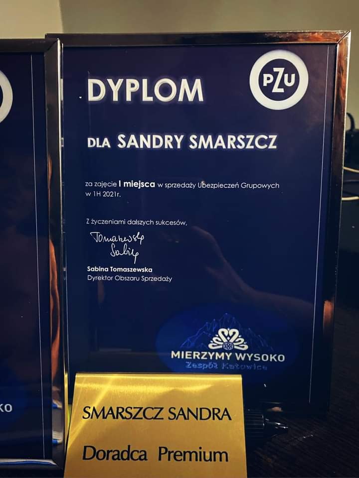 Dyplom dla Sandry Smarszcz z Katowic za zajęcie I miejsca w sprzedaży ubezpieczeń grupowych w 1H 2021 roku, wręczony przez PZU i Zespół Katowice, obok wizytówka Doradcy Premium.