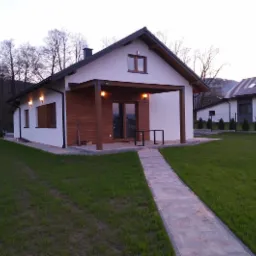 Nowoczesny dom jednorodzinny z drewnianą elewacją i zadaszonym tarasem w Wieprzu, widok z ogrodu, z kamienną ścieżką prowadzącą do wejścia.