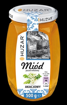 Słoik miodu akacjowego marki Huzar z etykietą przedstawiającą tradycyjną pasiekę i kwiaty akacji.