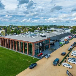 Zdjęcie z lotu ptaka nowoczesnego budynku biurowo-usługowego z elementami cegły, z dużym parkingiem i zadbanym trawnikiem.