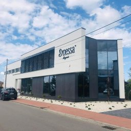 ITB Biuro Inżynierskie Piotr Kurasiński - Nowoczesny budynek usługowy z dużymi oknami i logo firmy na elewacji, biało-szara kolorystyka, widok z zewnątrz, zadbany teren wokół budynku.