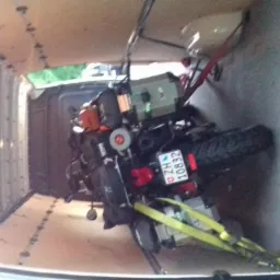 Motocykl zabezpieczony pasami wewnątrz furgonetki z drewnianą podłogą, widoczna tablica rejestracyjna ZG 10832.