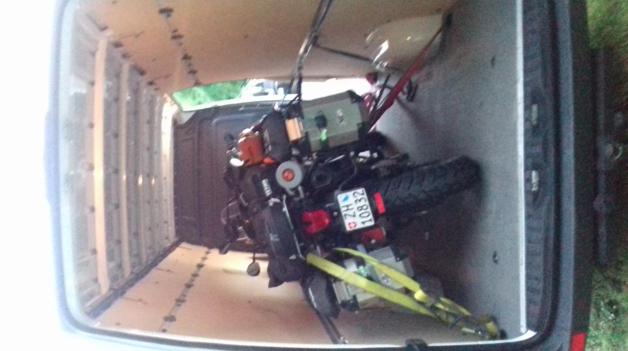 Motocykl zabezpieczony pasami wewnątrz furgonetki z drewnianą podłogą, widoczna tablica rejestracyjna ZG 10832.