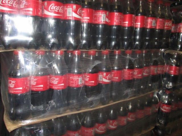 Paleta napojów gazowanych w plastikowych butelkach, owinięta folią stretch, widoczne czerwone etykiety z białym logo.