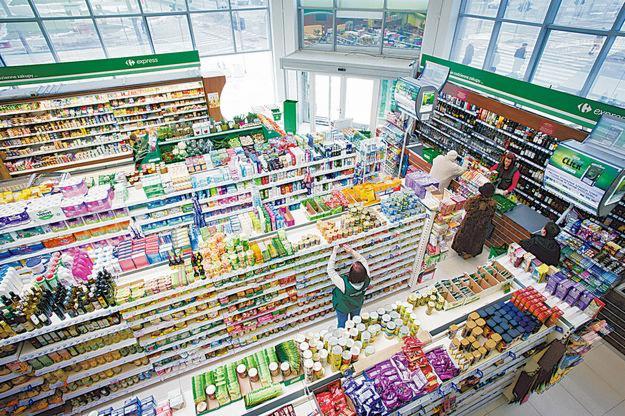 Wnętrze sklepu spożywczego Carrefour Express z perspektywy z góry, ukazujące półki pełne różnorodnych produktów, w tym napojów alkoholowych, oraz klientów robiących zakupy.