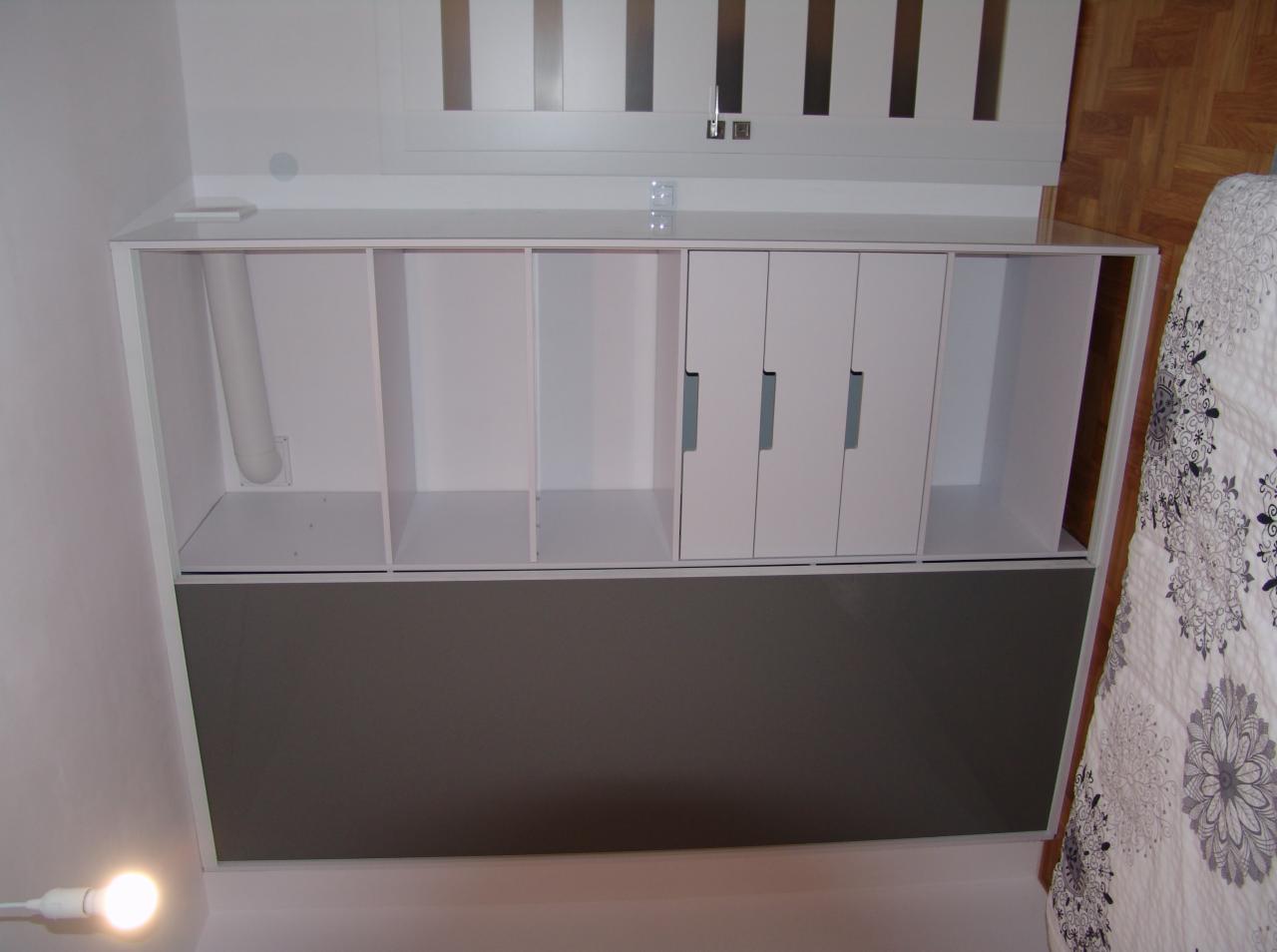 Biała zabudowa meblowa z szarym panelem dolnym, składająca się z otwartych półek i szafek z podłużnymi uchwytami, widoczna z dołu pod kątem.