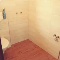 Wykończona kabina prysznicowa z beżowymi płytkami imitującymi kamień na ścianach, drewnopodobną podłogą z odpływem liniowym i widoczną armaturą.