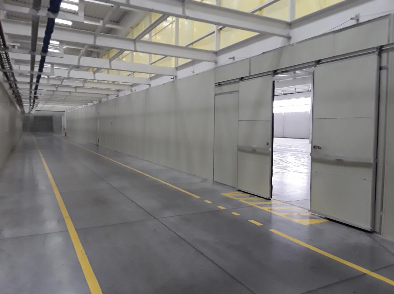 Wnętrze hali magazynowej z przesuwnymi drzwiami, widoczne żółte linie na posadzce oraz konstrukcja sufitu