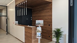 Recepcja w nowoczesnym biurze z drewnianą okładziną ściany, oświetleniem punktowym i stojakiem na ulotki informacyjne.