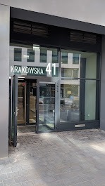 Wejście do biura z adresem Krakowska 41, widoczne przez szklane drzwi obrotowe, jasne wnętrze w tle.