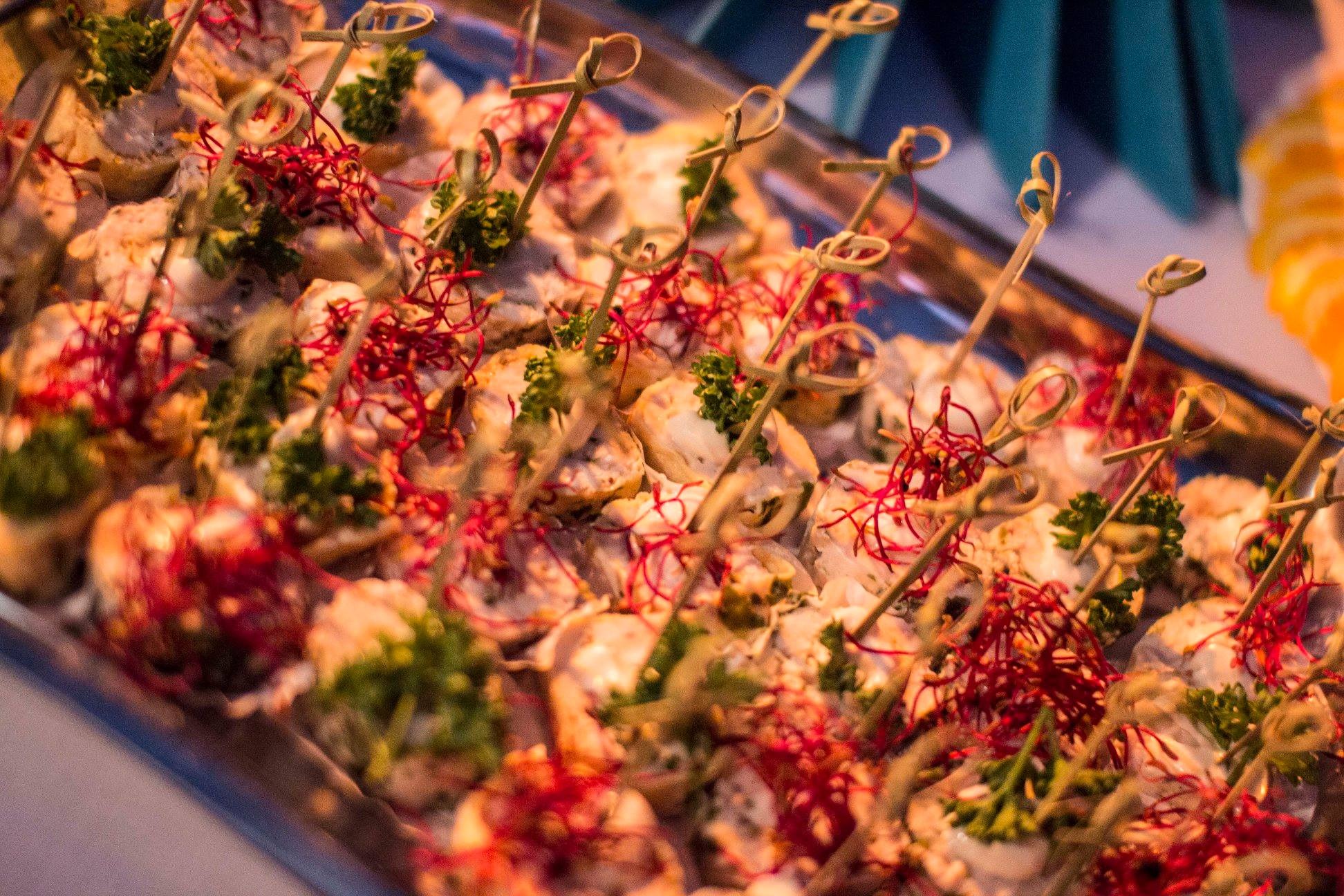 Taca z roladkami przystawkowymi na przyjęciu, udekorowanymi czerwoną mikro zieleniną i zieloną pietruszką, spięte bambusowymi wykałaczkami z pętelką.