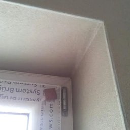 RAF-BUD Rafał Lisek - Narożnik okna po tynkowaniu maszynowym, widoczna struktura tynku i zabezpieczona rama okienna.