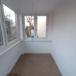 Jasne wnętrze pokoju po remoncie z nowymi oknami VEKA, świeżo pomalowanymi ścianami na biało i podłogą ułożoną w jodełkę. Widoczne wystające kable ze ściany.