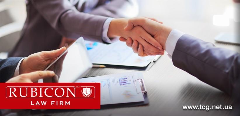 Uścisk dłoni nad stołem z dokumentami i tabletem, symbolizujący zawarcie umowy, w tle widoczne analizy i wykresy.