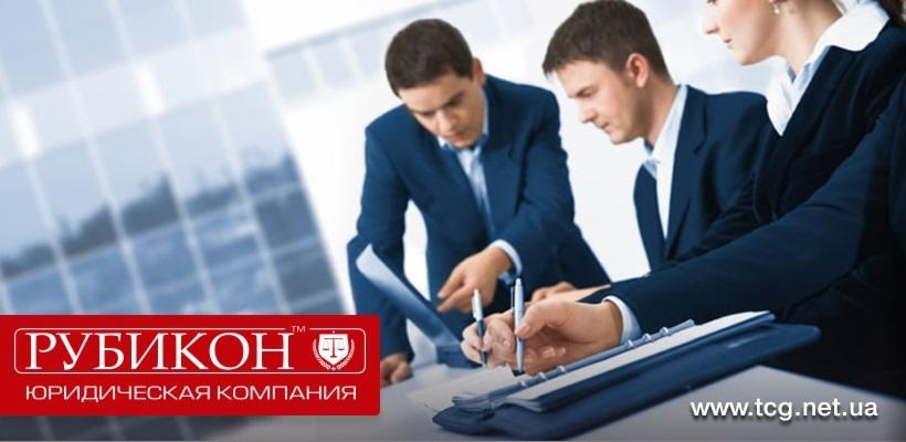 Trzech prawników w garniturach omawia dokumenty, jeden z nich wskazuje palcem na laptopa, drugi robi notatki na podkładce z kartkami, w tle widoczny budynek z przeszkleniami.