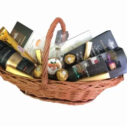 Wiklinowy kosz wypełniony kawą Davidoff, czekoladkami Ferrero Rocher, pralinkami Anthon Berg w kształcie butelek, czekoladą i innymi słodyczami, całość na białym tle.