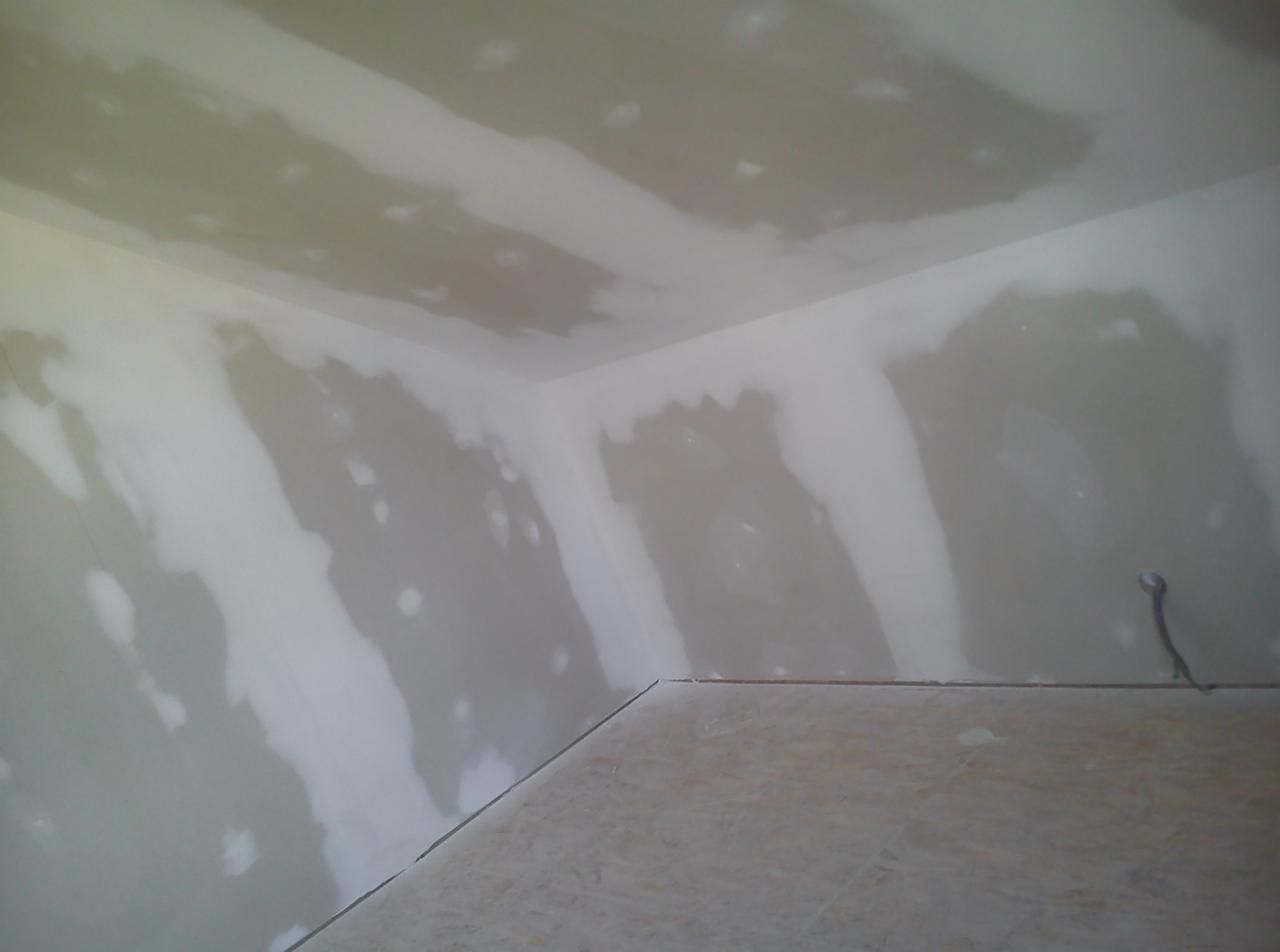 Ściany i sufit w trakcie szpachlowania w pomieszczeniu w Krynica-Zdrój, widoczne nierównomierne warstwy gładzi gipsowej, przygotowanie do dalszych prac wykończeniowych.