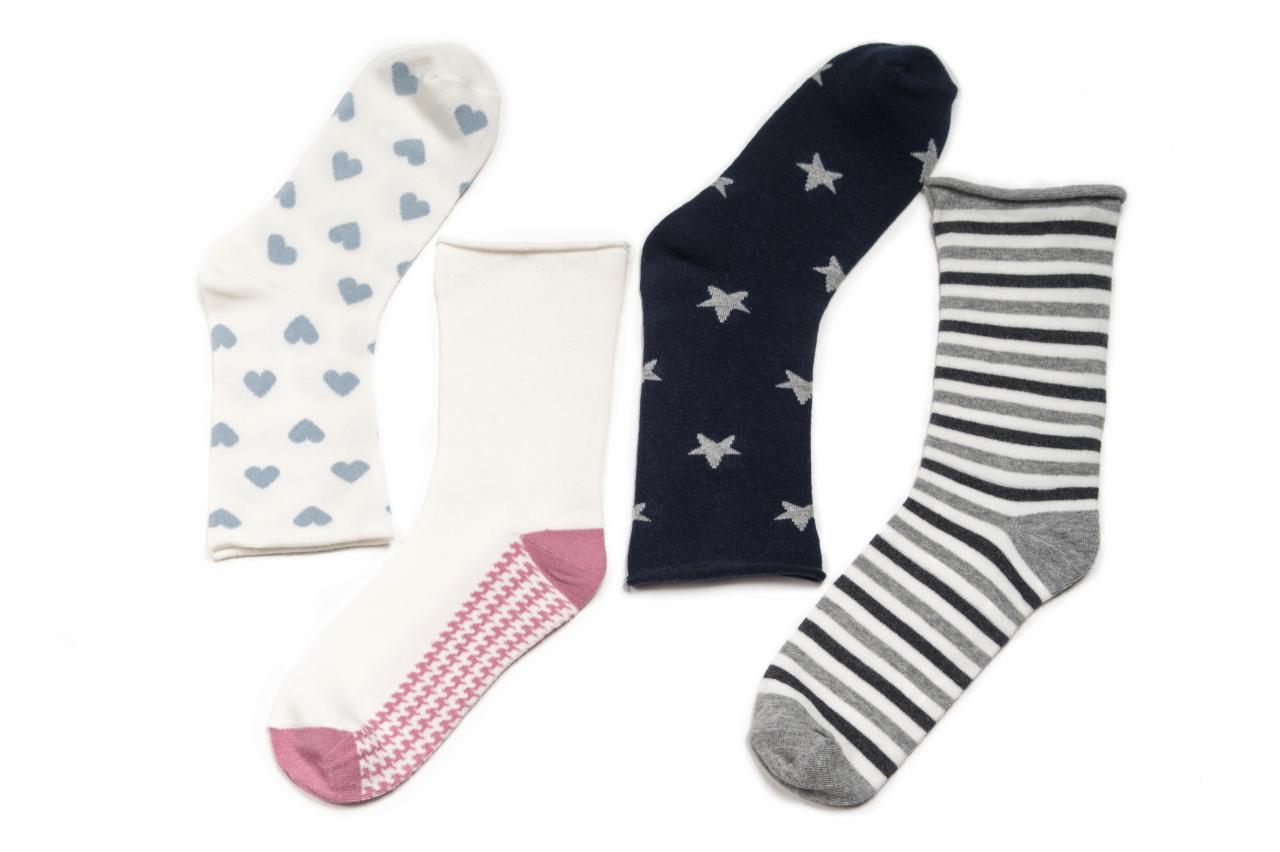 Cztery pary różnorodnych skarpetek: białe w błękitne serca, białe z różowym wzorem w jodełkę, granatowe w srebrne gwiazdki, szaro-białe w paski, ułożone na białym tle.