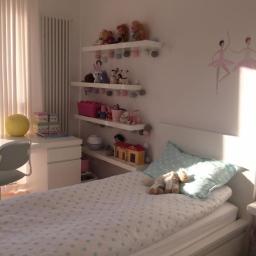 tdesign - Pokój dziecięcy z białymi meblami, półkami z zabawkami i naklejkami baletnic na ścianie, oświetlony popołudniowym słońcem.