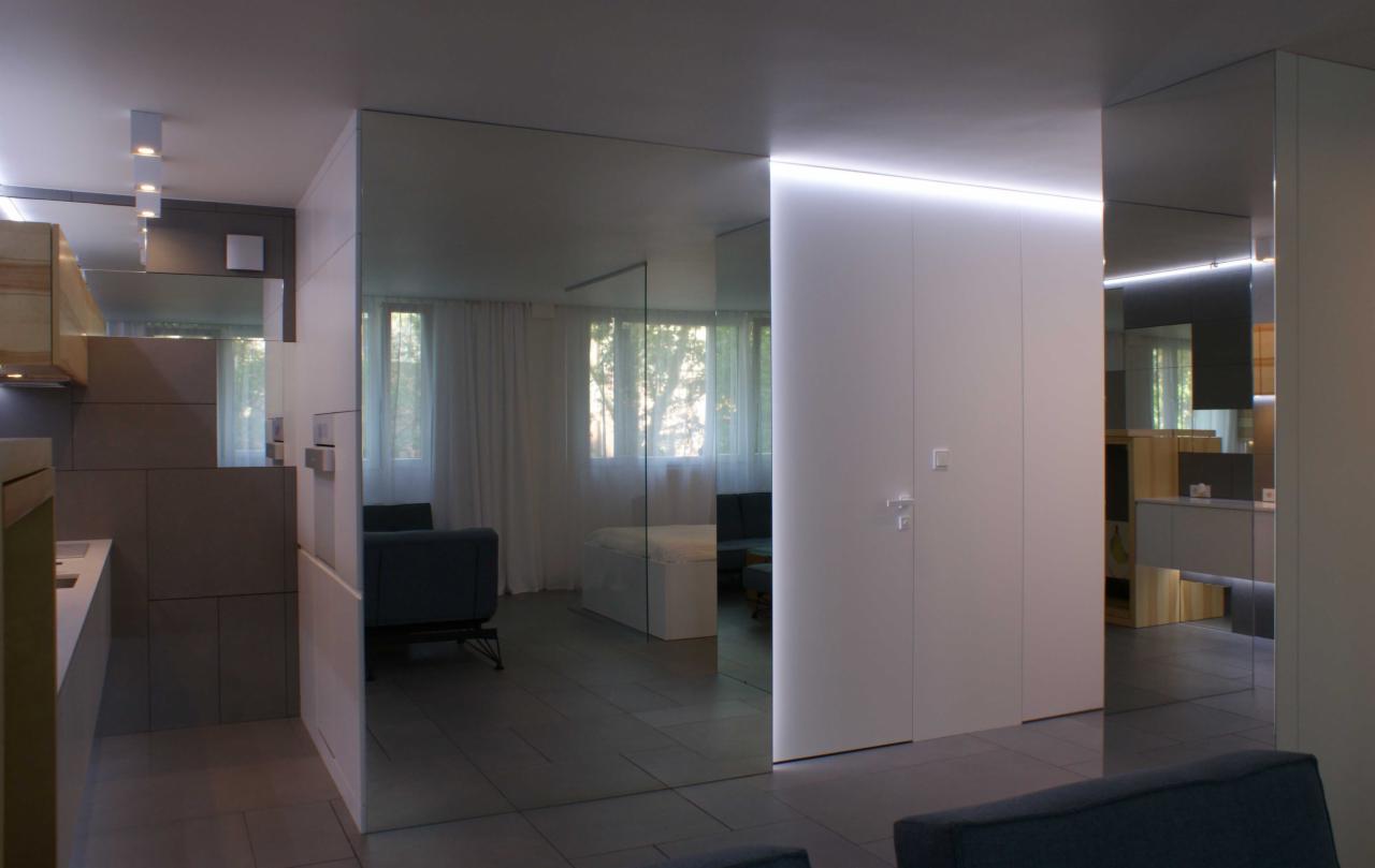 Nowoczesne wnętrze mieszkania z lustrzanymi ścianami, minimalistyczną kuchnią i salonem w tle, oświetlenie LED pod sufitem.